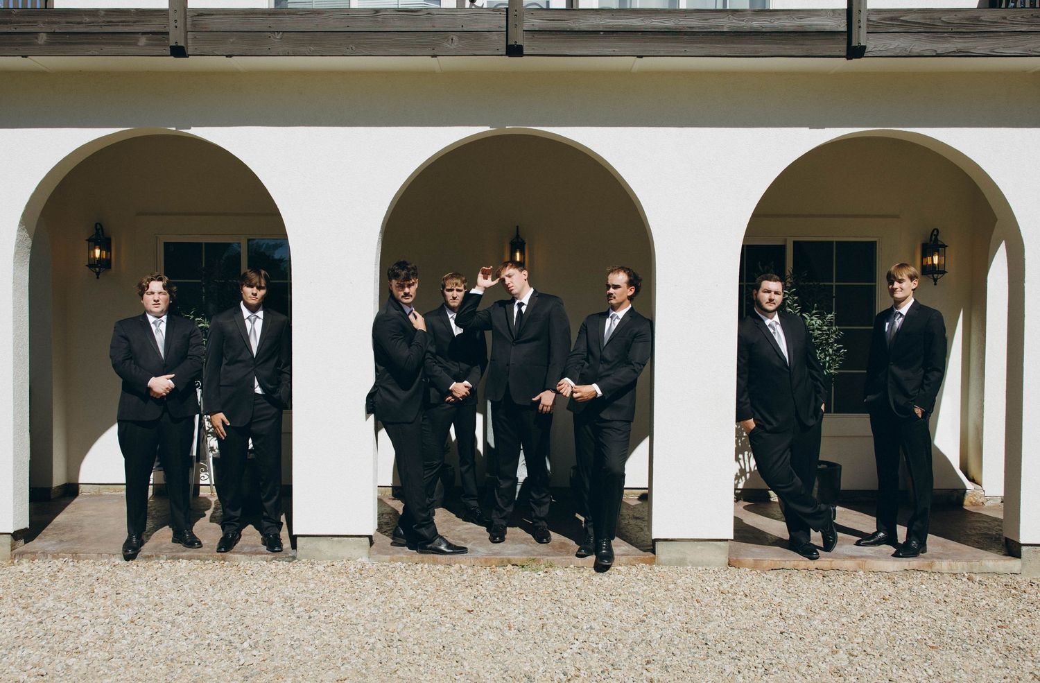 A group of formally dressed people standing under white arched colonnades in elegant suits and formal attire.
