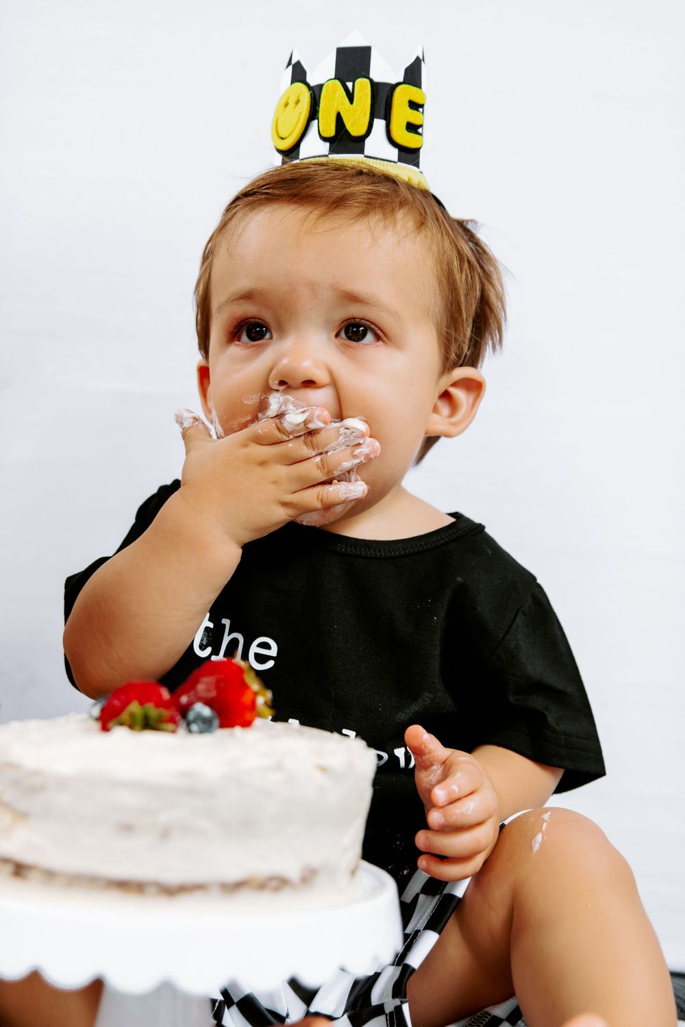 Small child wearing a crown getting messy while eating birthday cake with white frosting.