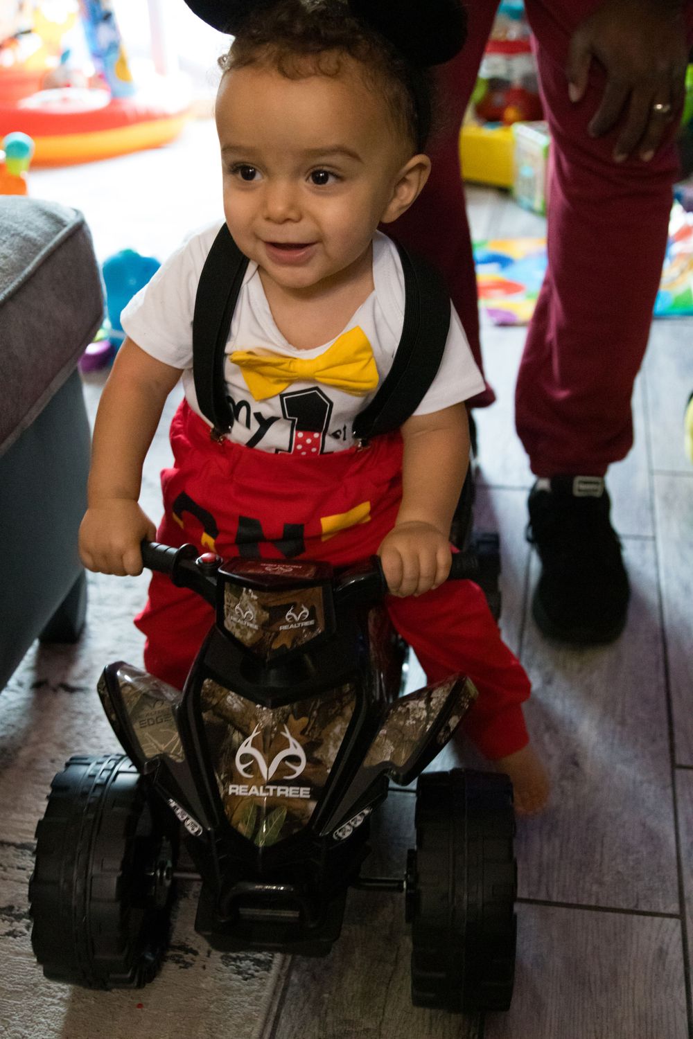 A small child rides on a black toy ATV quad wearing red pants and a white t-shirt.