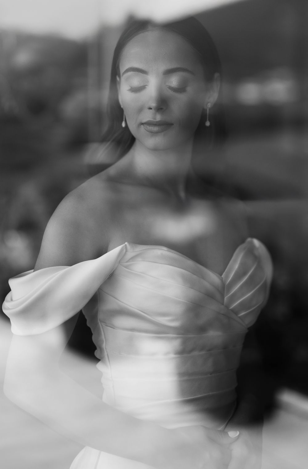 A dreamy black and white portrait shows a person in a strapless white gown with their eyes closed in a serene pose.