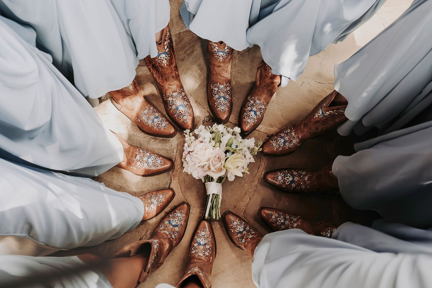 A beautiful circle of brown leather cowgirl boots with flowers on them surrounding a bridal bouquet