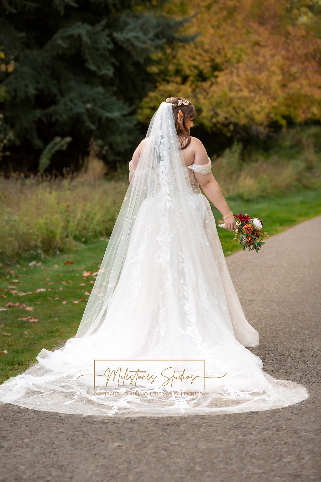 back of bridal gown with cathedral length veil bride looking down to right at bouquet