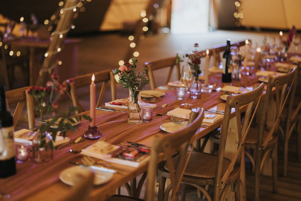 A rustic wooden dining table set for a wedding reception with string lights overhead at Scrivelsby Walled Garden.