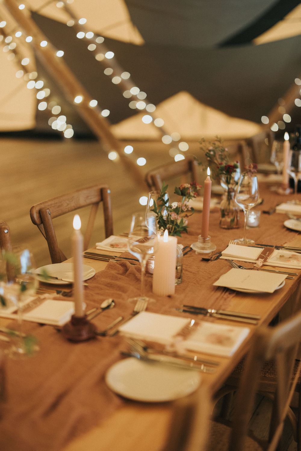 Wooden dining table set with elegant place settings under warm string lights for an intimate wedding reception at Scrivelsby Walled Garden.