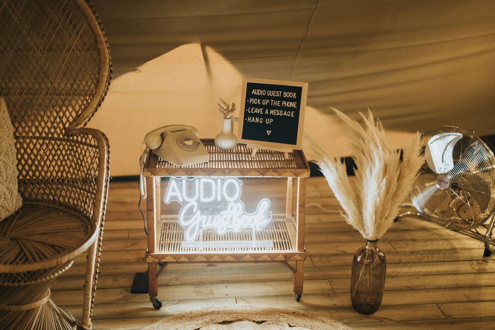 Illuminated audio booth sign with boho decor including wicker chairs and pampas grass in rustic wedding setup at Scrivelsby Walled Garden.