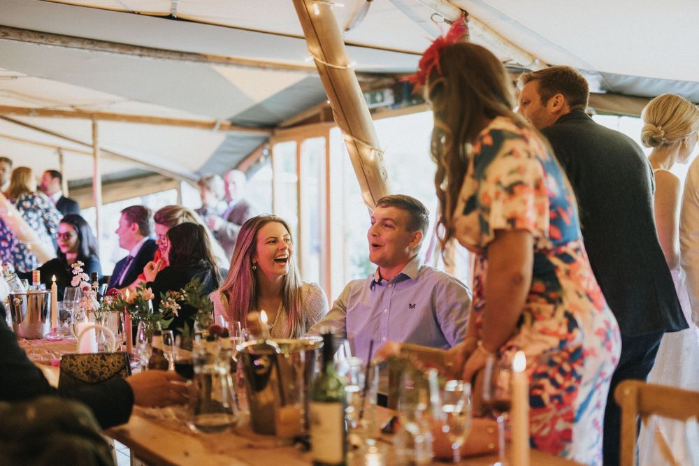 Guests enjoying a lively celebration in a wedding marquee tent with wine glasses and decorative lighting at Scrivelsby Walled Garden.