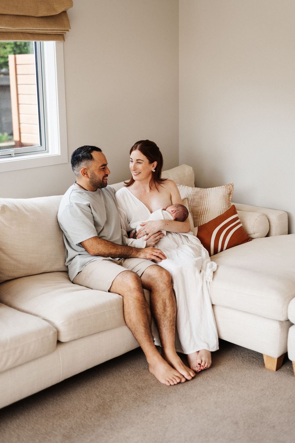 Four connected images show a couple relaxing intimately together on a white sectional sofa in a bright modern living room.