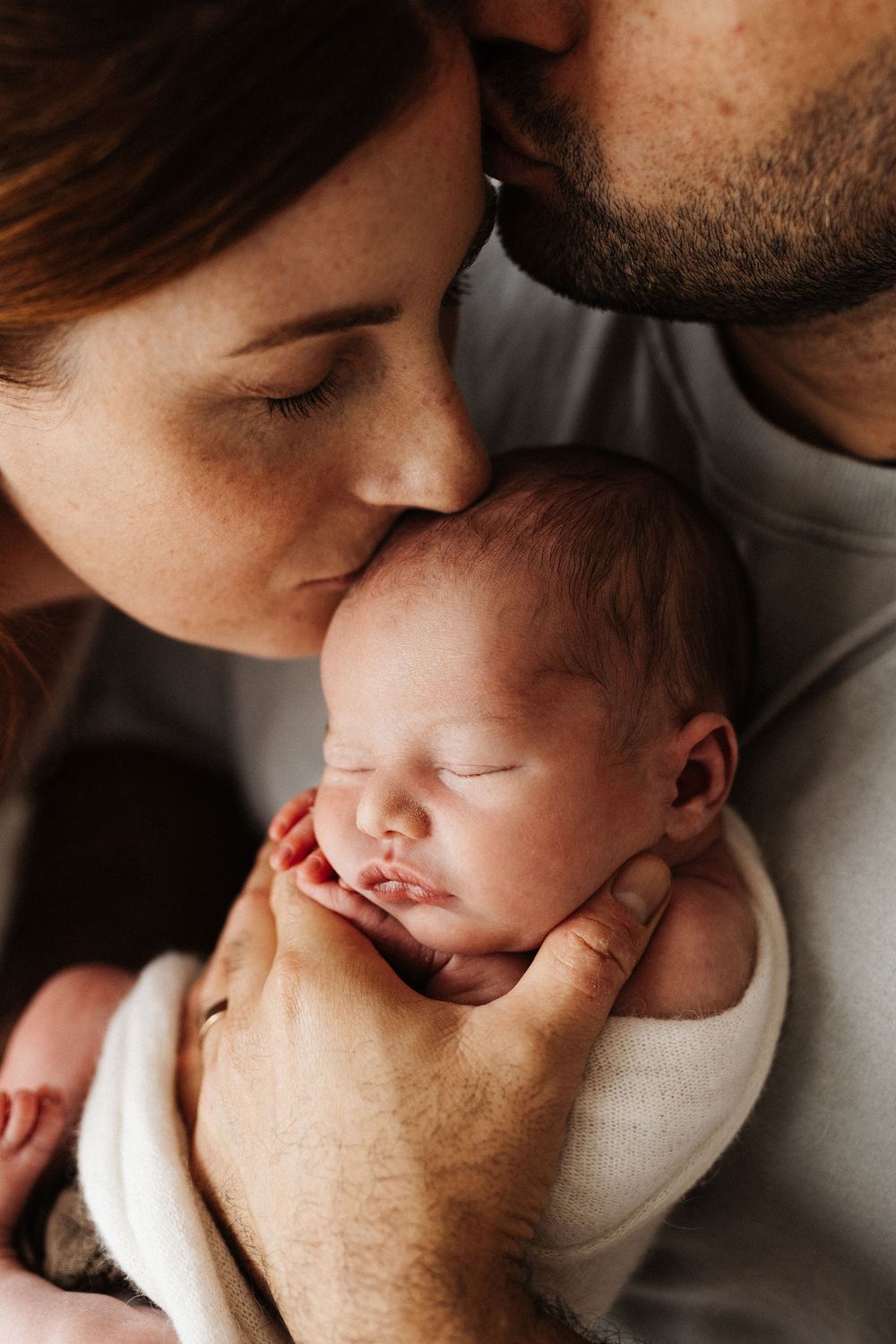 Parents sharing tender moment with sleeping newborn baby in intimate close-up.