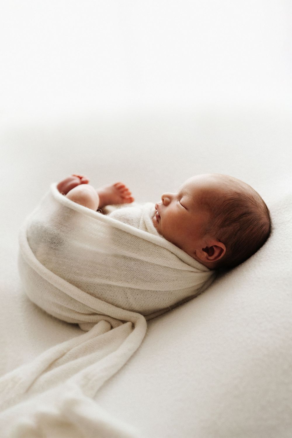 Sleeping newborn baby wrapped in white swaddle on light background.