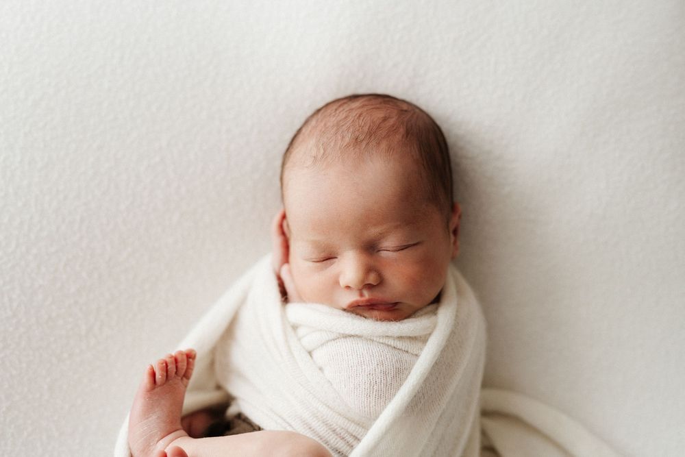 Newborn baby peacefully sleeping while wrapped in white swaddle.