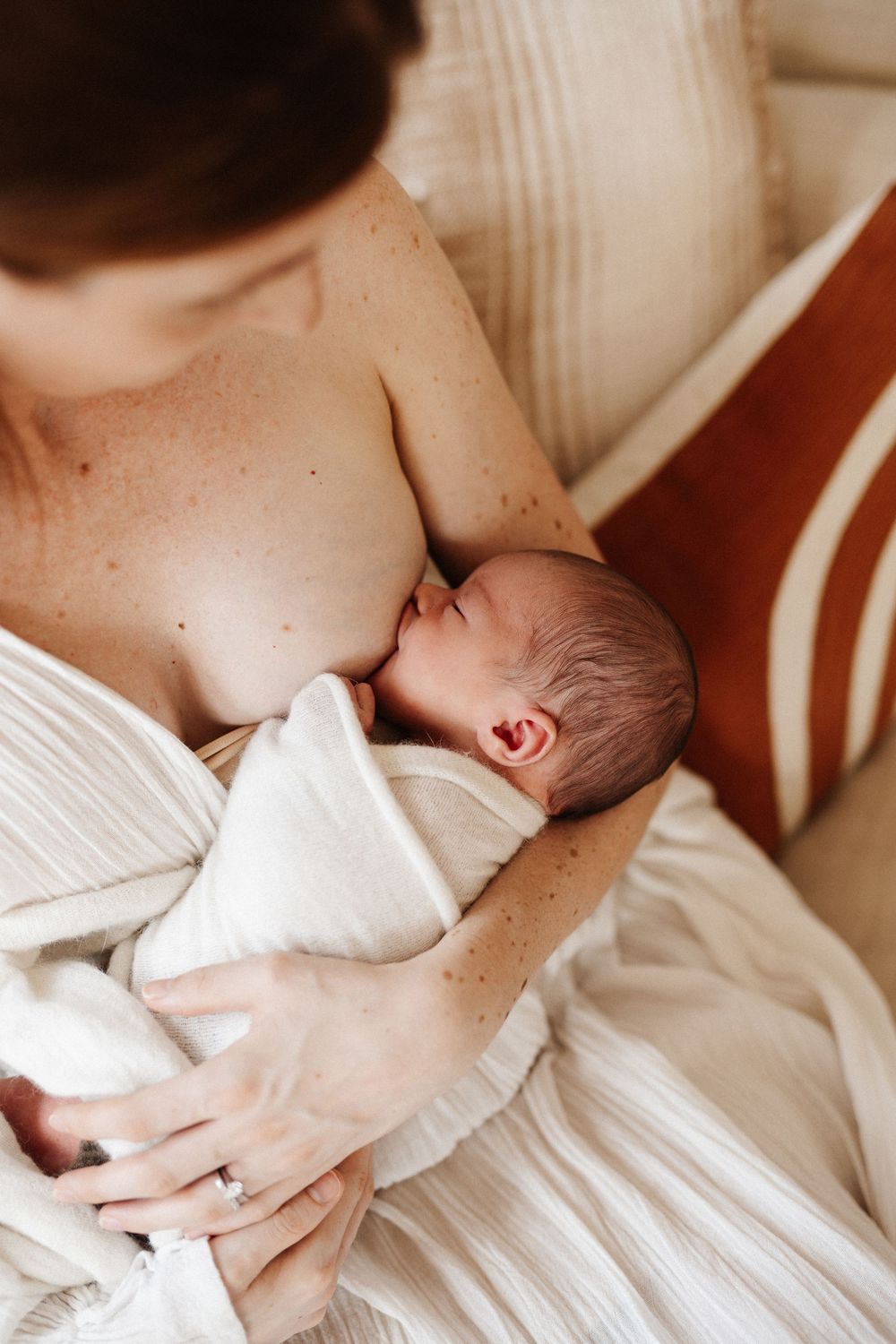 Intimate moment of newborn baby breastfeeding while wrapped in soft white fabric.