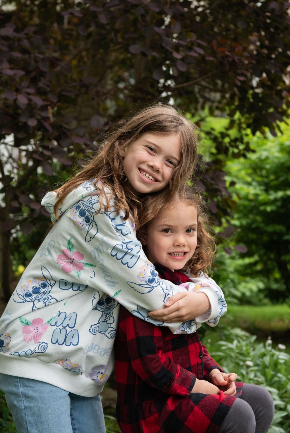 Two young girls in casual outfits share a playful moment while hugging outdoors.