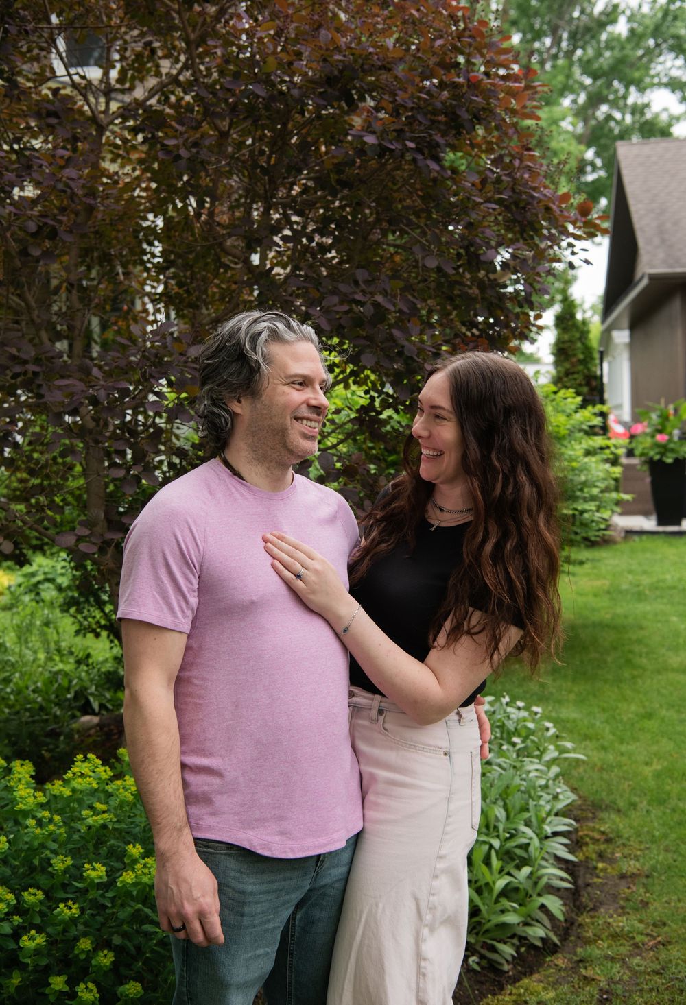 A couple shares a tender moment in a garden with blooming trees in the background.