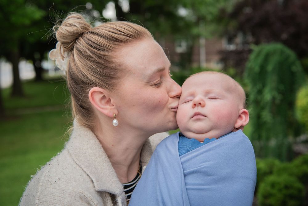 Parent giving gentle kisses to baby dressed in light blue clothing outdoors.