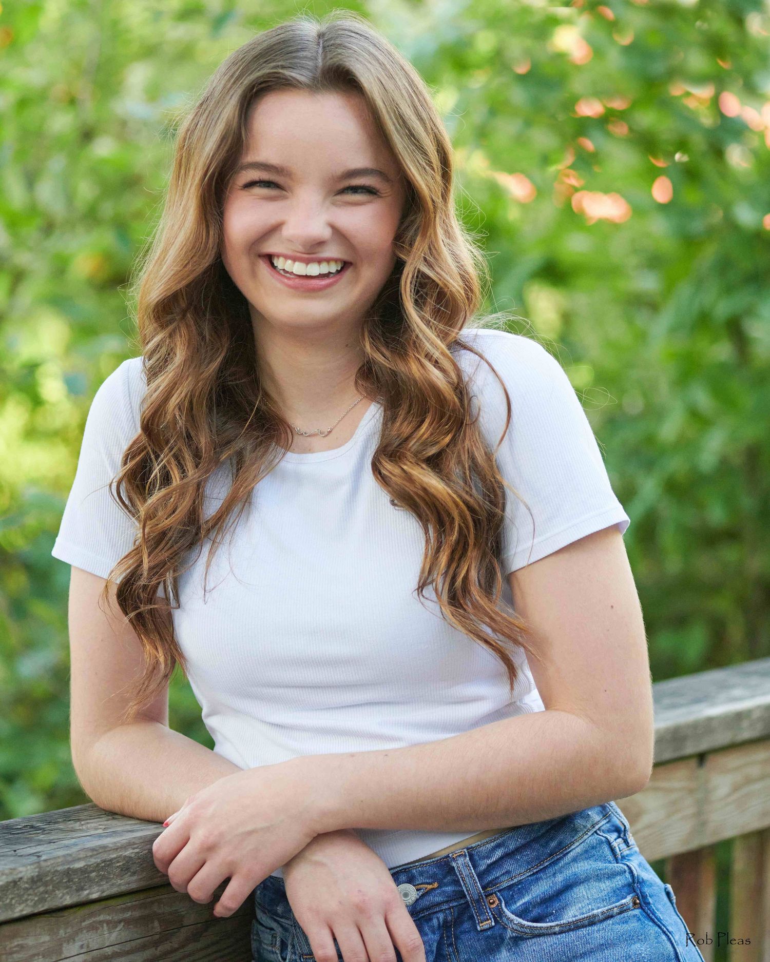 high school senior female smiling while leaning against wooden bridge railing at Decoursey Park.