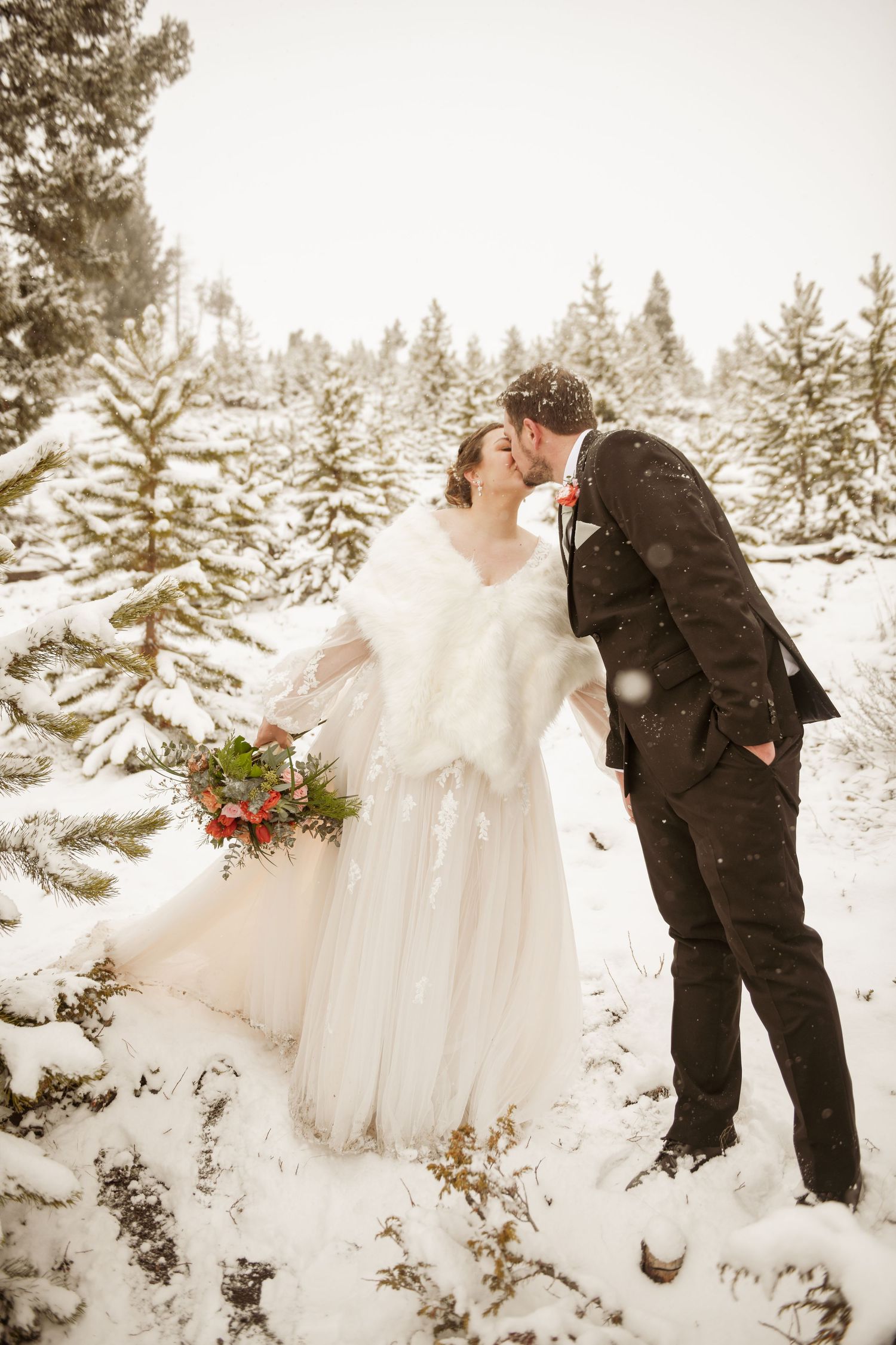 A bride and groom share a romantic winter wedding photoshoot in a snowy evergreen forest.