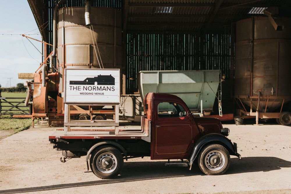 Vintage delivery truck parked outside rustic wooden buildings with textured brown and green siding.