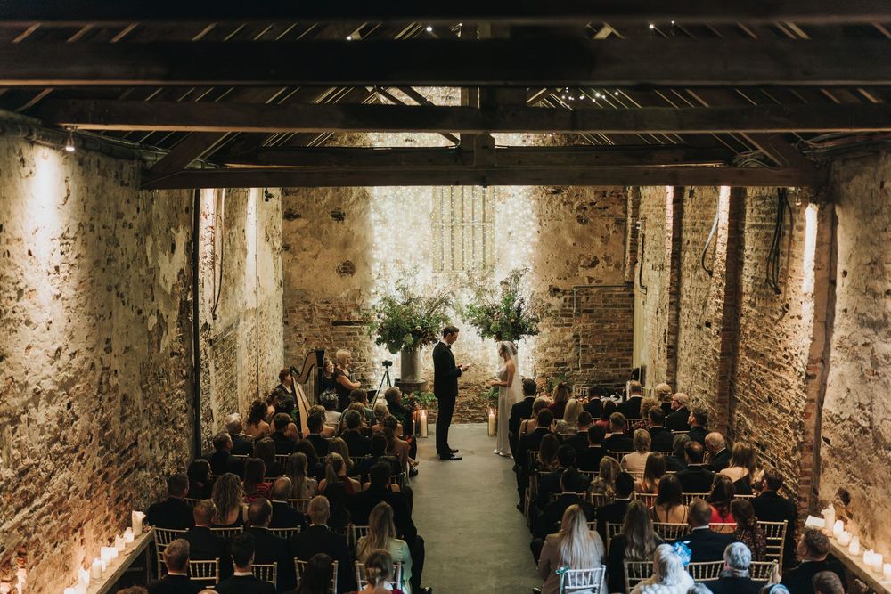 Wedding ceremony taking place in rustic stone venue with exposed brick walls and wooden beams overhead.