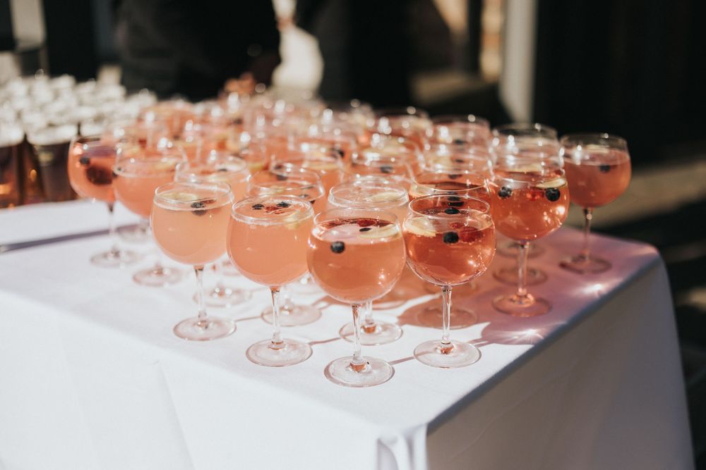 Rows of coupe glasses filled with pink cocktails arranged elegantly on a white tablecloth at an event.