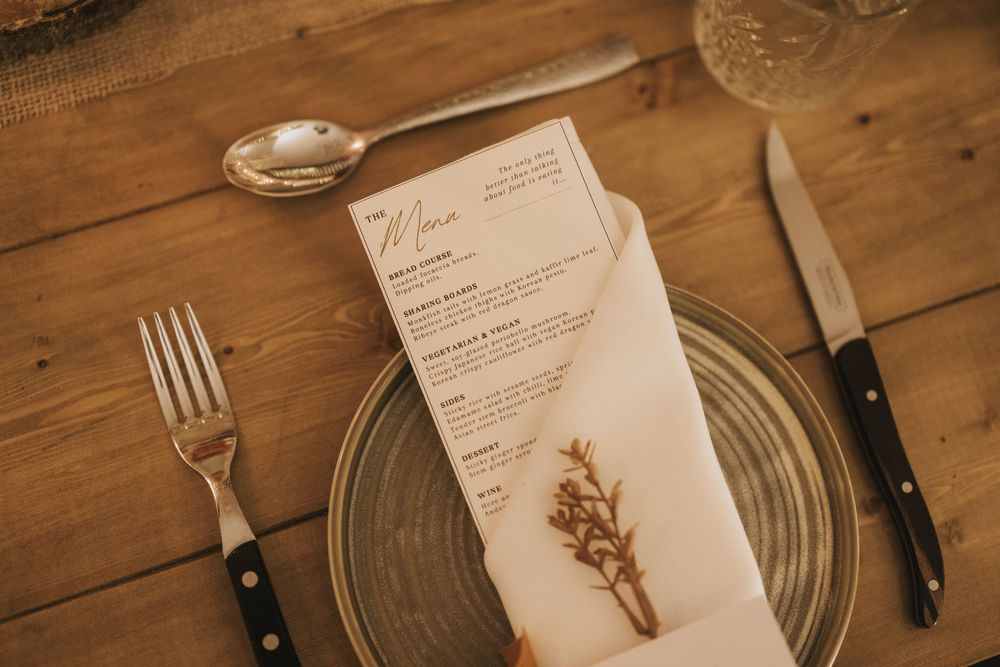 Elegant rustic place setting with glass, silverware, and menu on a wooden table featuring romantic details.