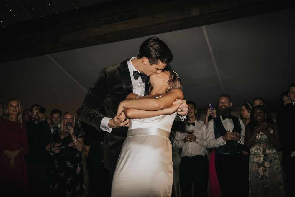Couple sharing a romantic dance together at an evening wedding reception with guests watching from the background.