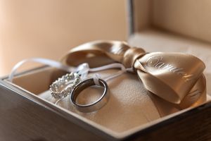 Wedding accessories including rings and jewelry arranged on a textured beige surface.