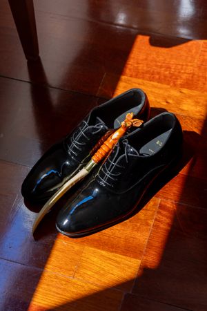 Black formal dress shoes positioned on polished wooden flooring with dramatic lighting.