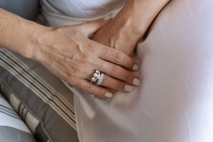 Close-up of hands wearing an elegant engagement ring against white fabric.