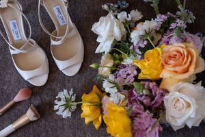 Colorful wedding bouquet with yellow, pink and purple flowers arranged next to white bridal shoes.