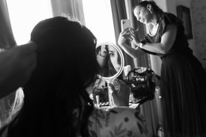 Black and white candid wedding preparation scene with natural window lighting.