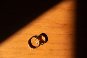 Wedding rings casting dramatic shadows on wooden surface in warm lighting.