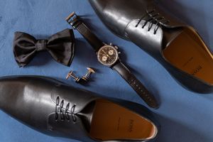 Collection of formal black dress shoes and accessories arranged on blue background.