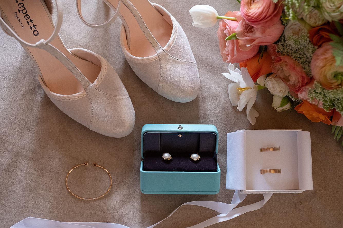 Wedding accessories including white shoes, jewelry, and rings displayed with coral flowers.