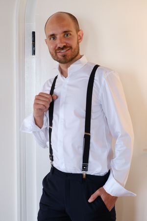 Formal attire featuring white dress shirt with black suspenders against white wall.