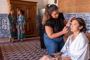 Makeup artist working on client in room with decorative blue tile walls.