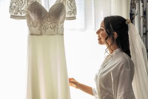 Wedding preparation scene with elegant white dress hanging in window light.