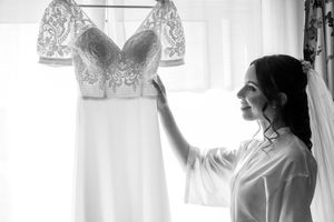 Black and white photo of wedding dress preparation by window.