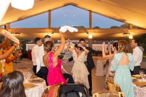 Wedding reception guests dancing and celebrating under a tent with warm lighting.