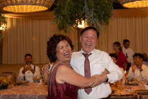 Wedding guests laughing and dancing at reception under warm lighting.