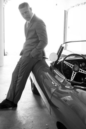 Black and white photos of someone in a suit posing with a classic vintage car.