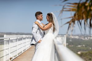 Romantic moment between newlyweds on a sunny balcony overlooking a scenic landscape.