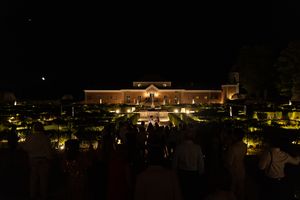 Illuminated building at night with crowd of spectators gathered on lawn for outdoor event.