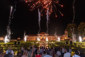 Fireworks display over elegant building with formal gardens and crowd watching festivities.