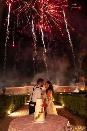 Wedding cake and couple silhouetted against dramatic fireworks display at elegant venue.