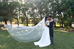 Elegant wedding portrait with bride's veil flowing in garden setting.