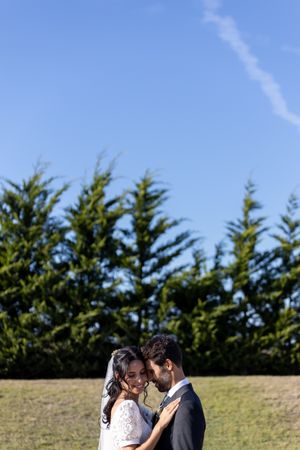 Newlyweds share an intimate moment against a backdrop of evergreen trees.