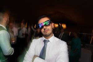 Party guest in sunglasses and tie poses at nighttime wedding reception.