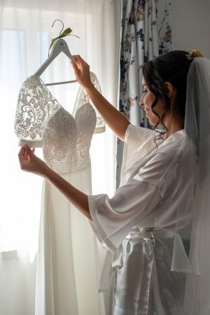 A white lace wedding dress hanging on display while being admired in morning light.