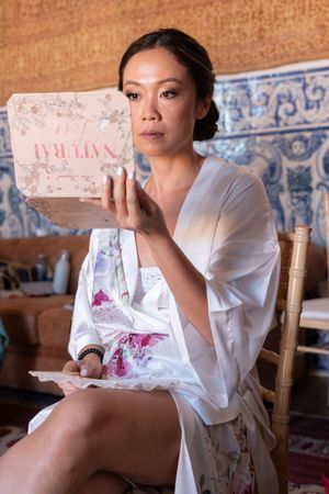 A person in a silk robe holding a decorative box while sitting in a room with blue tiled walls.