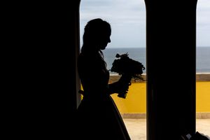 Dramatic silhouette of bride against arched window with ocean view.